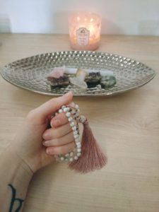 Meditation mala in hand, Candle, and crystals.